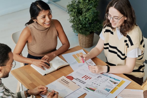 Three people at a table with papers showing graphs and notes